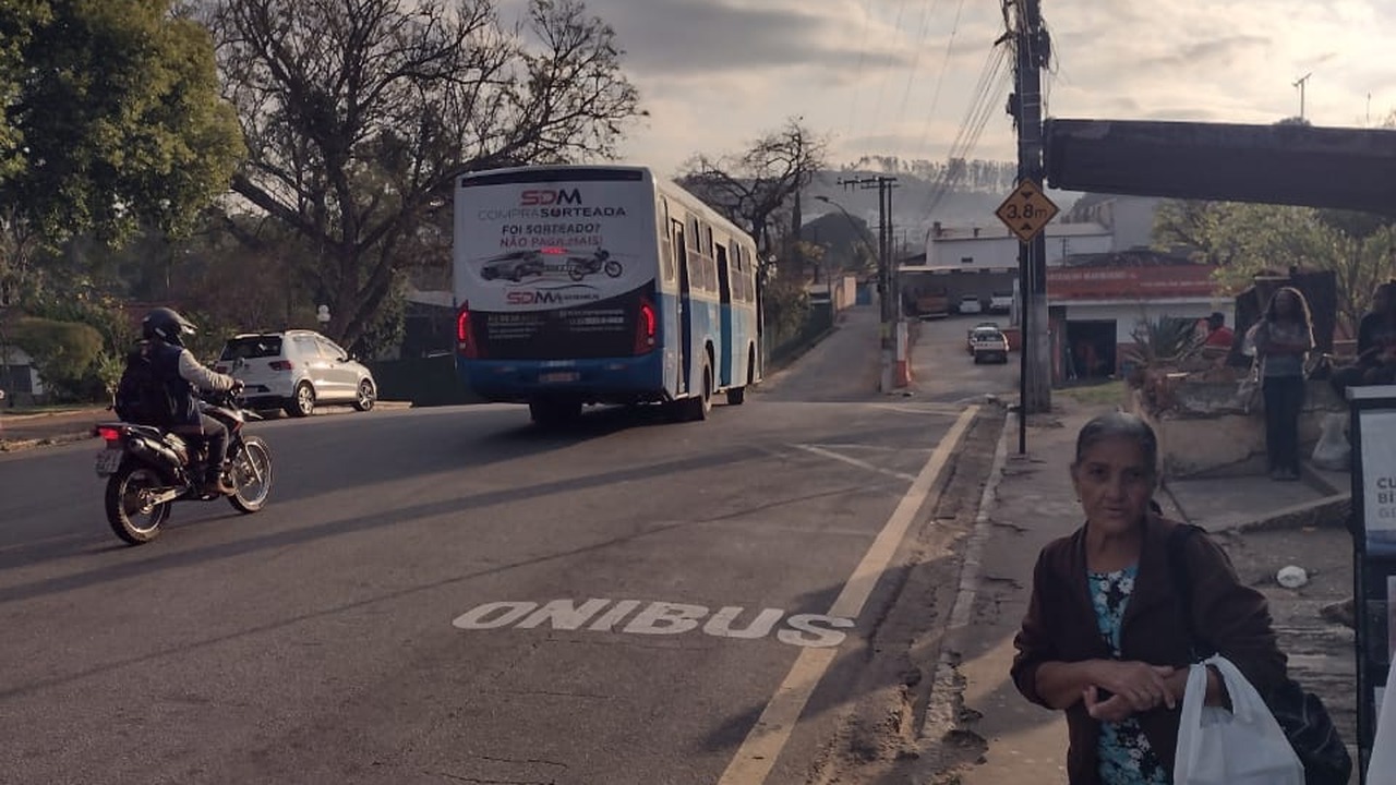 Passageira aguarda no ponto enquanto o ônibus se afasta, na região da Praça da Estação, em Lavras.