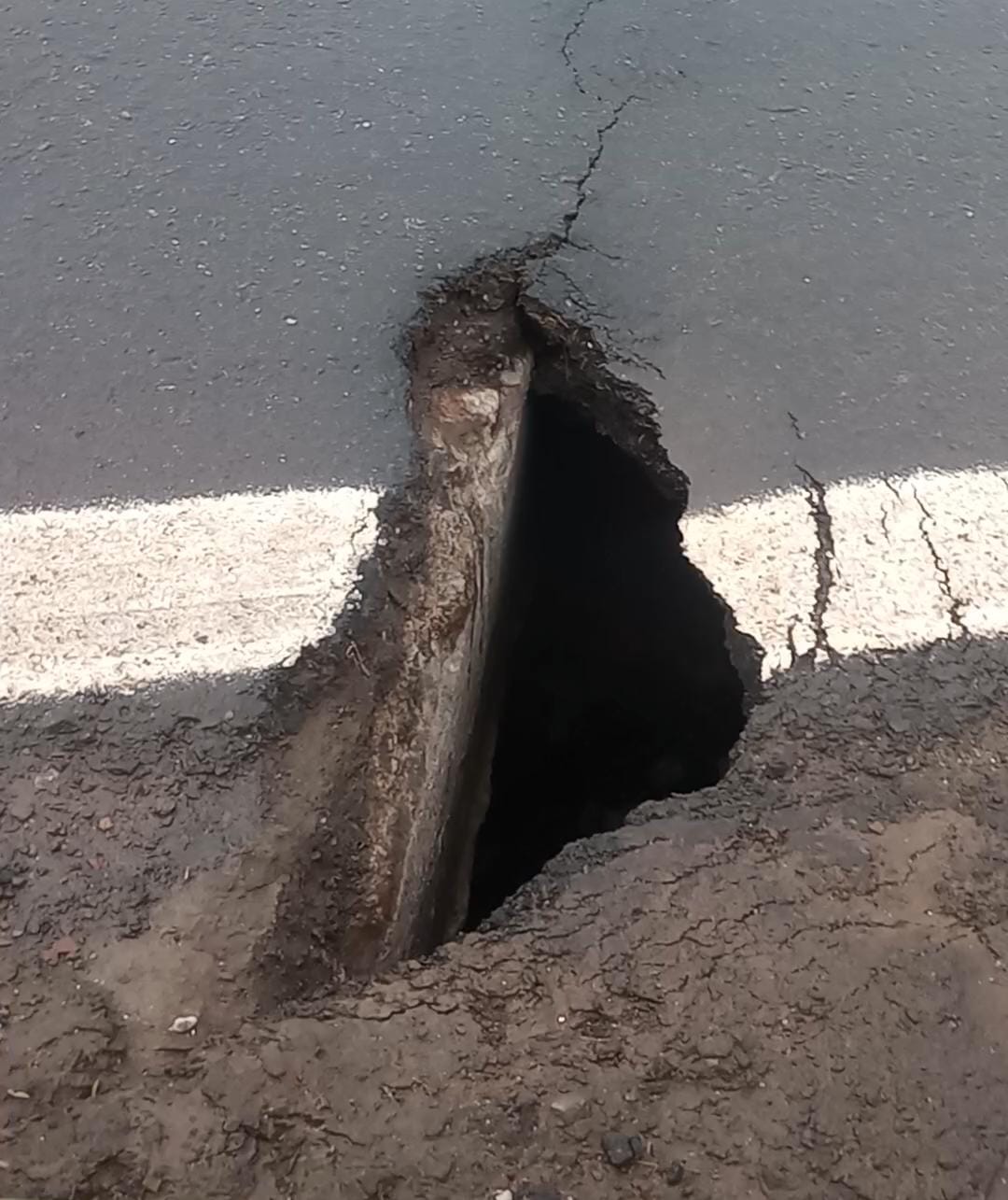 Buraco aberto no asfalto da BR-265, ao lado da faixa de sinalização da pista.