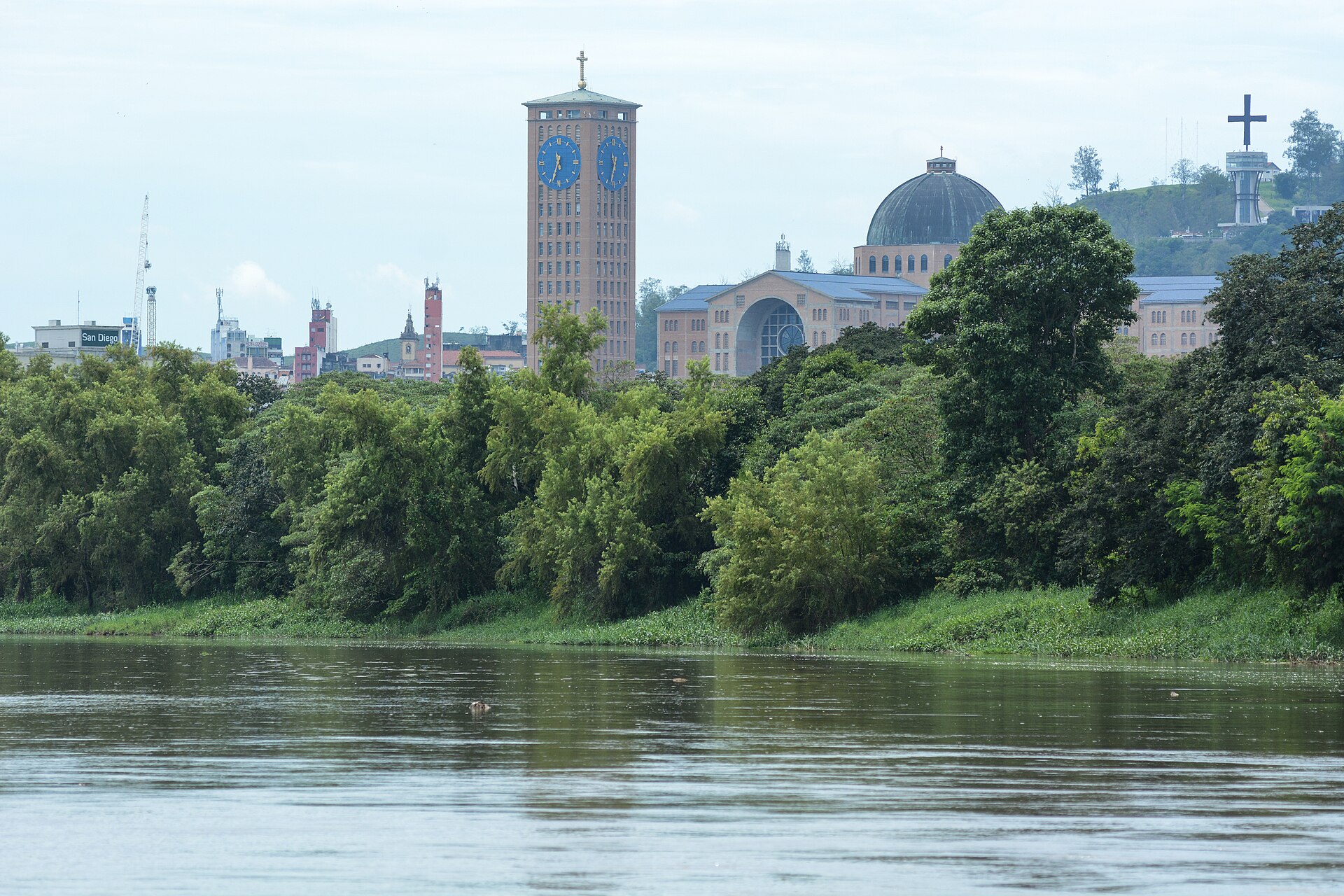 O Porto Itaguaçu, no rio Paraíba do Sul, onde a tradição situa o encontro da imagem, com a Basílica de Aparecida ao fundo. Foto: Marco Ankosqui/MTur Destinos